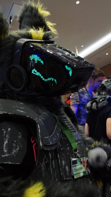 a grey and yellow protogen fursuit. wearing a scratched up armor and badges