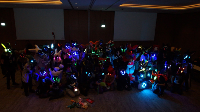 A groupphot of protogens and synths taken in the dark. The colorful suits lighting up the room