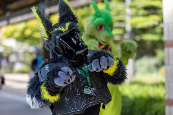 A yellow and grey protogen fursuit with a damaged visor. wearing grey, worn armor. Holding a stick of ram