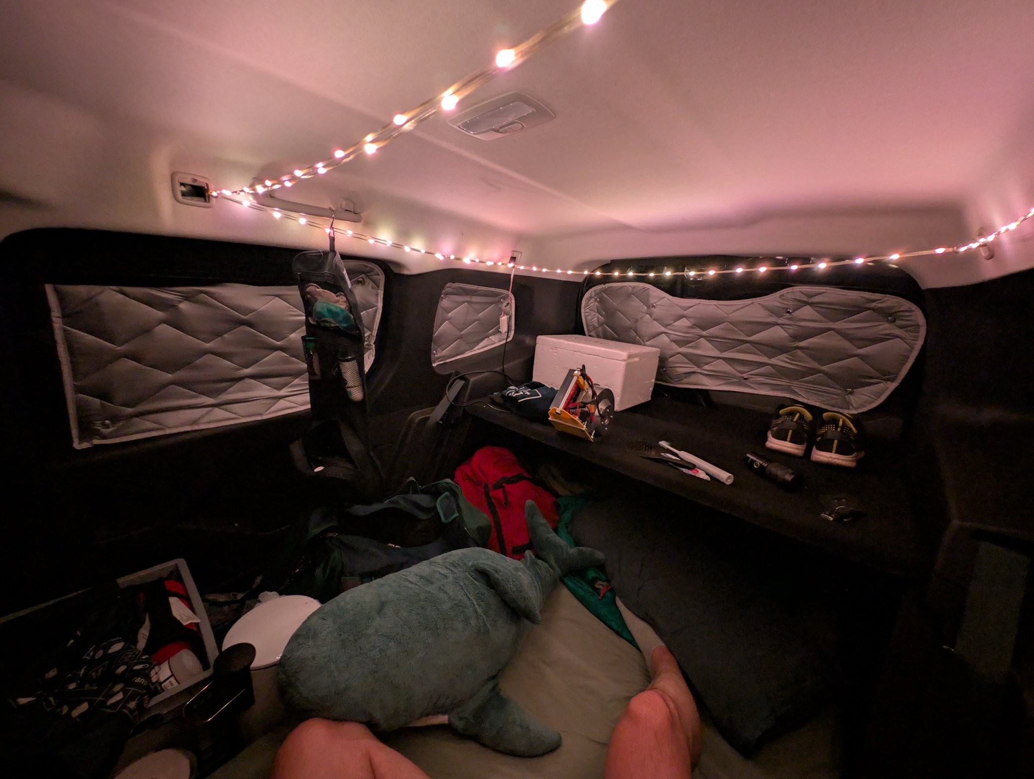 Inside of my car with warm white led string, a blahaj, mattress, pillow and some luggage