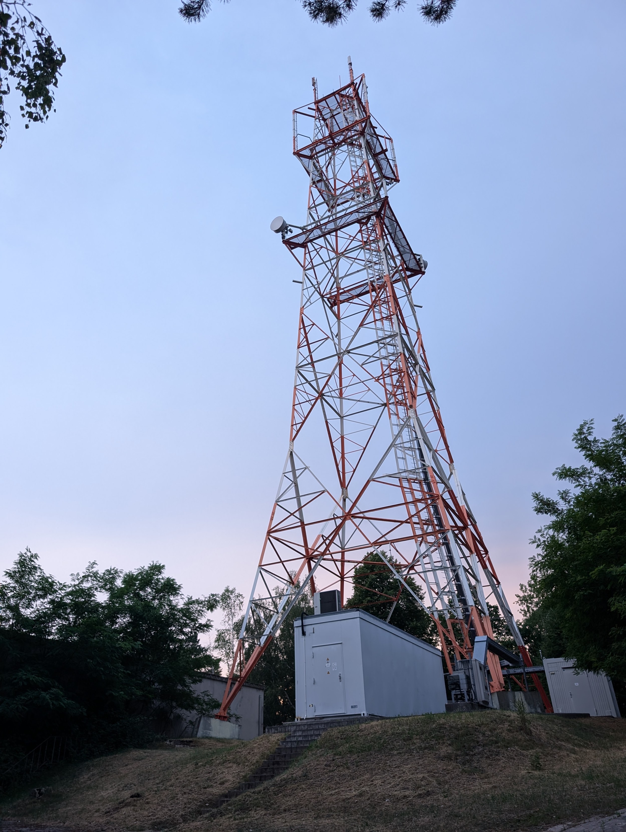 Red and white metal radio tower with a white container in front of it