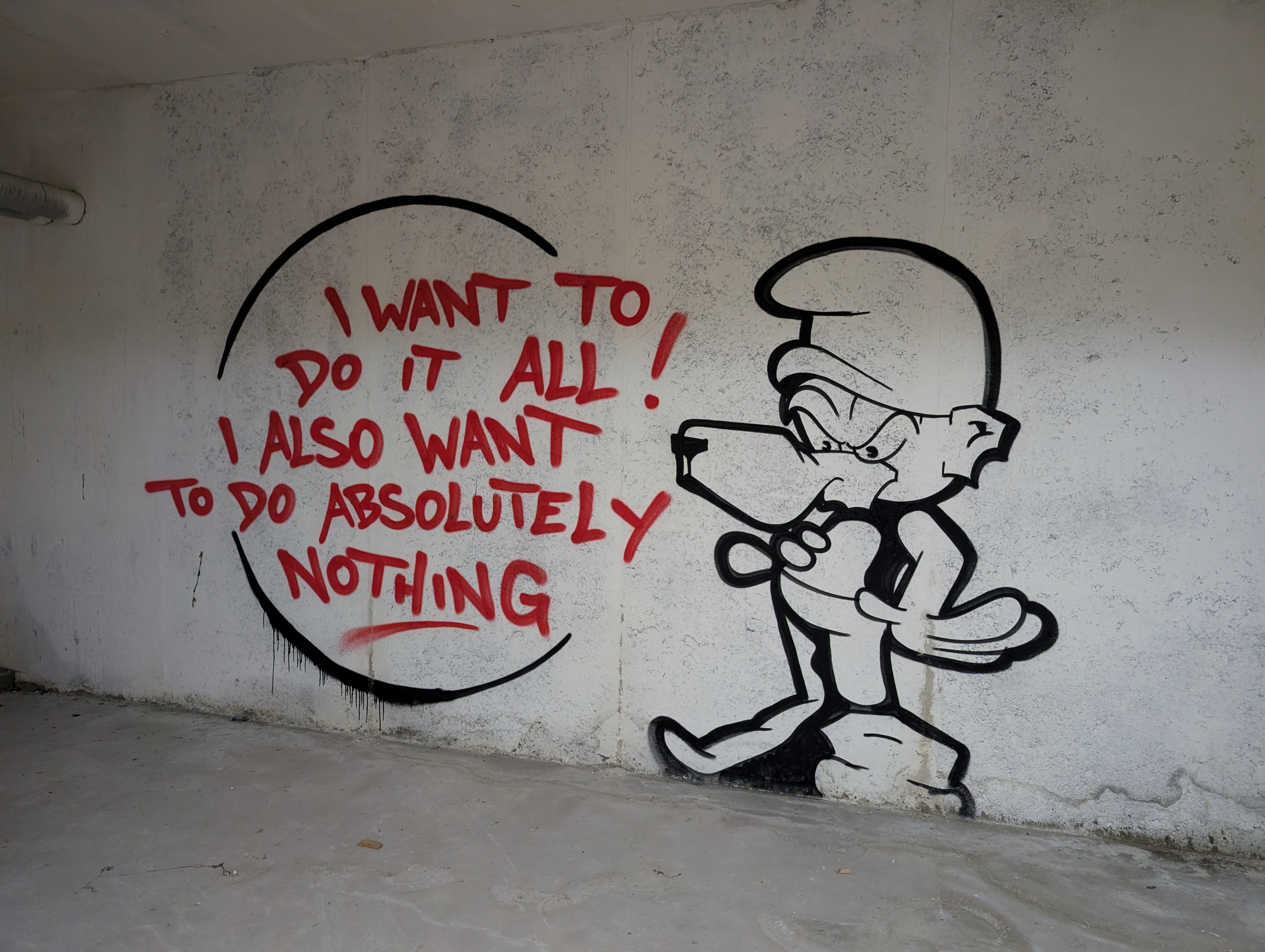 Black graffiti on a wall of a vaguely canine character wearing a beanie and saying, in red text: "I want to do it all! I also want to do absolutely nothing"