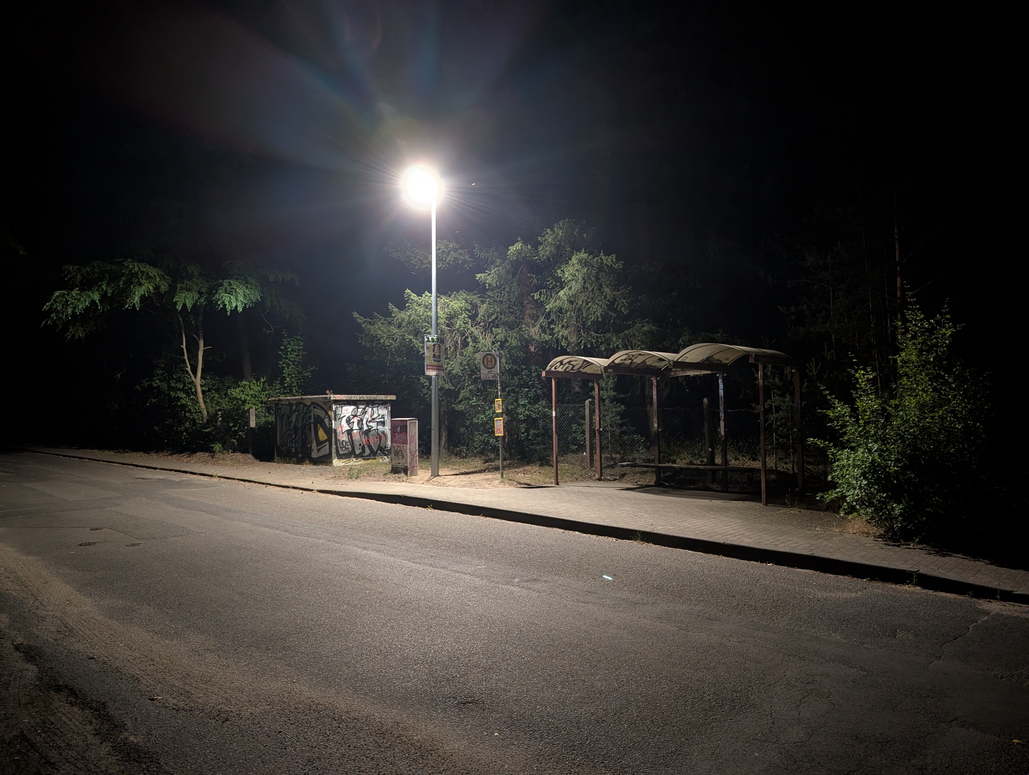 Dilapidated and graffiti covered bus stop with a single bright street light next to it