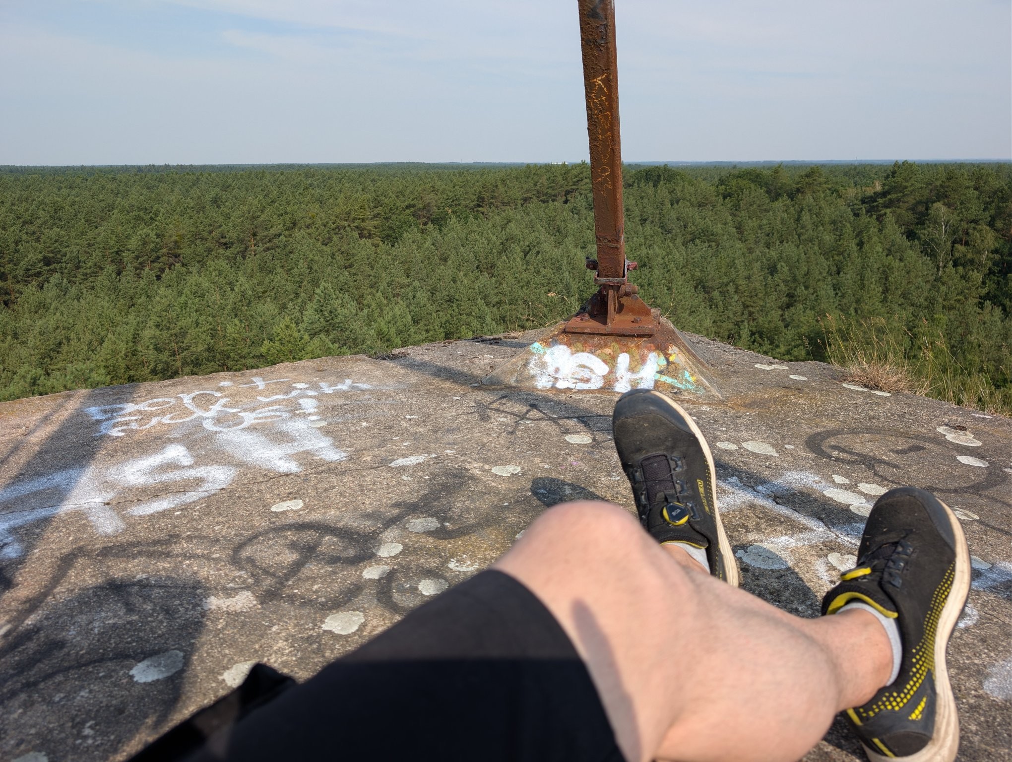 My legs crossed on the roof of some sort of tall structure, surrounded by trees up to the horizon