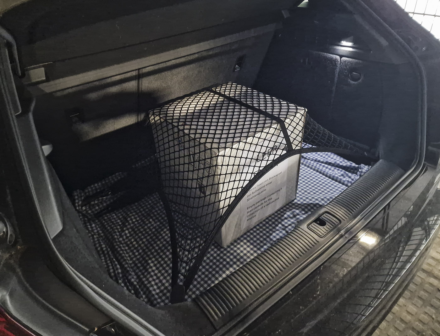 Photo of a hatchback's open trunk with a large, white, cardboard box sitting in the middle, firmly held in place by a cargo net.