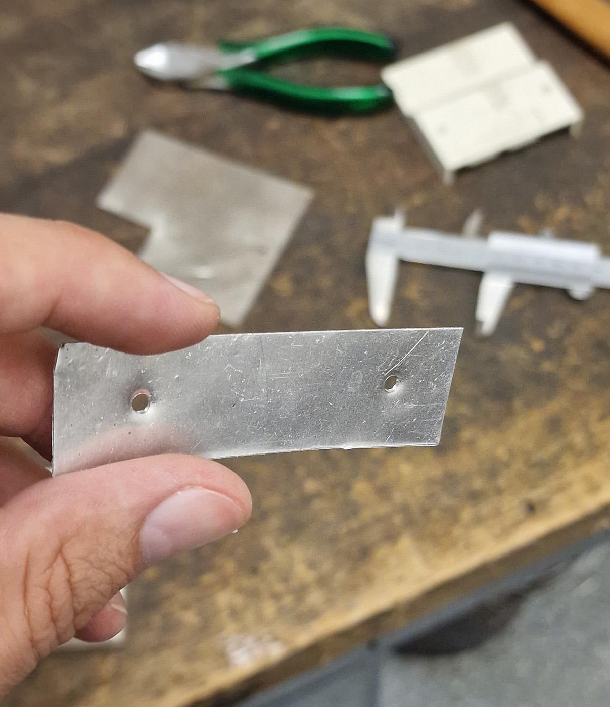 Photo of a thin piece of sheet metal that someone cut from a piece out of the parts box. Germans use the nice word "Grabbelkiste" for it, which I think is lovely. Someone also punched two holes into it, as this person was too lazy to switch on the drill for such a tiny job.