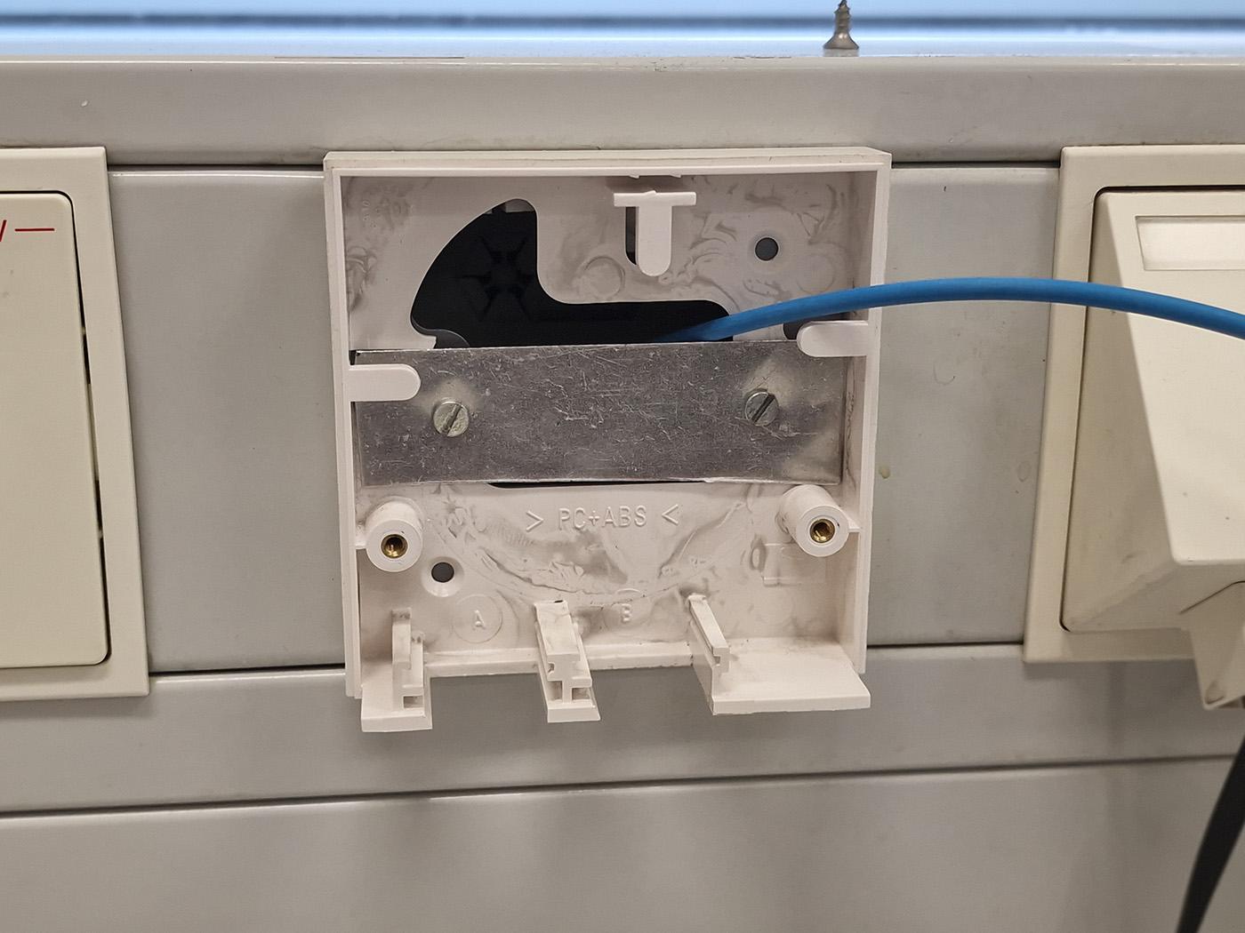 Photo of the broken junction box, with the parts that had fractured now being covered up by the thin strip of sheet metal, with latter attached to the original screw holes. The fact that it's thin and flexible also means that it won't put too much force on any part of the brittle 1999 plastic.