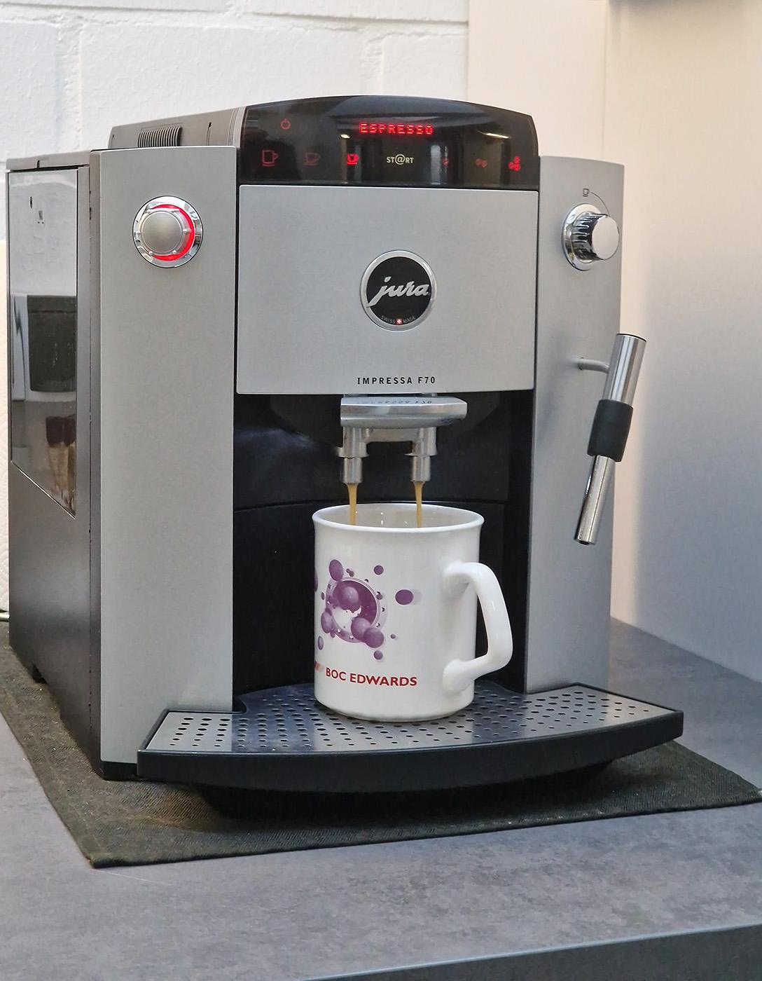 Photo of an ancient Jura Impressa F70 dispensing coffee into an Edwards-branded mug.
